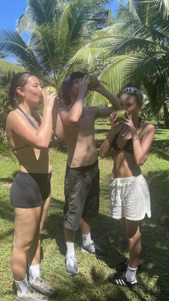 Two girls and a boy drink from coconuts