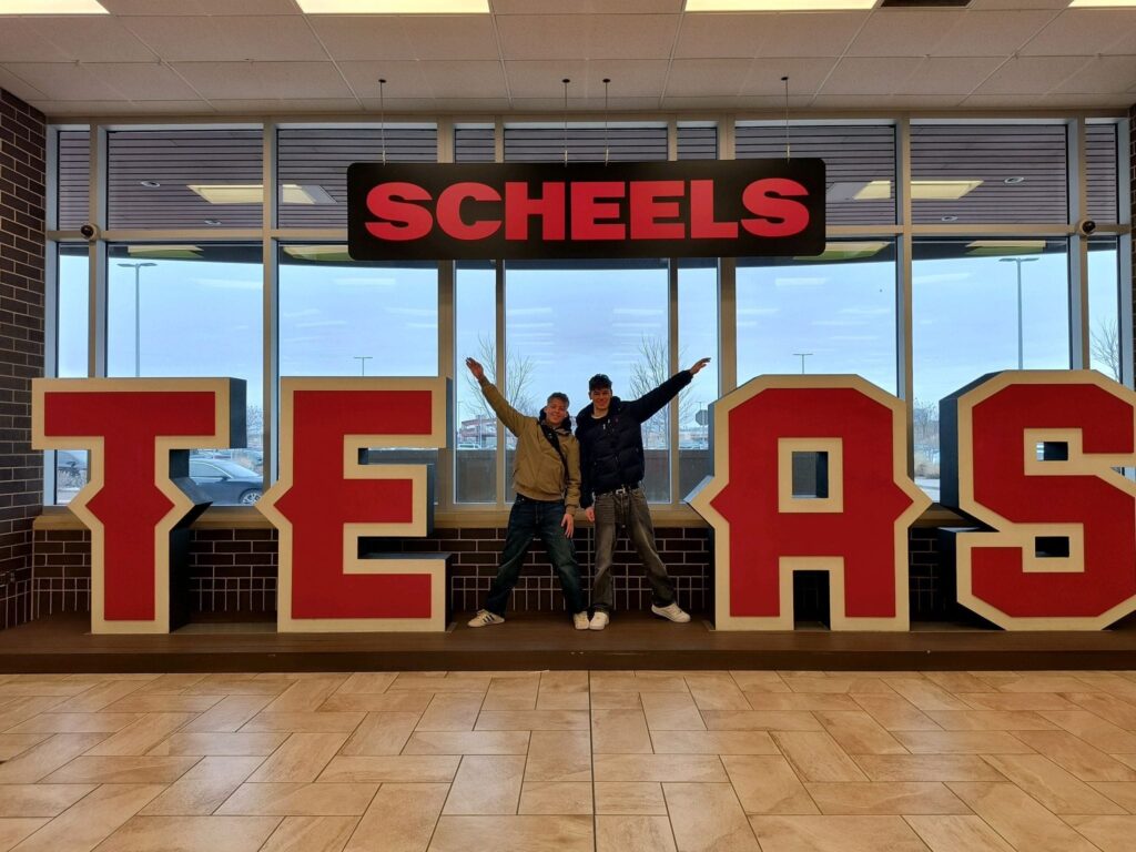 Two boys stand by a Texas sign and form the X in Texas themselves