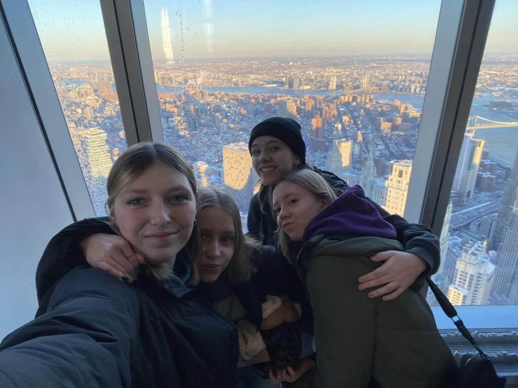 Fire piger står og tager selfie fra en høj bygning med udsigt iver byen