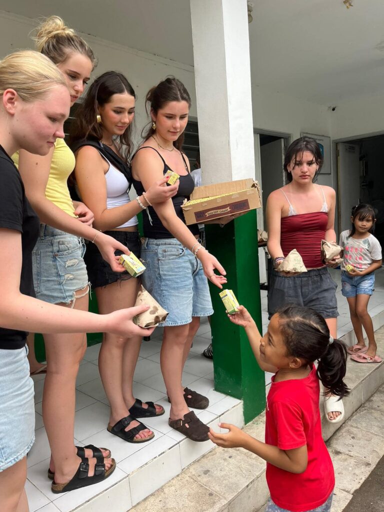 Danish girl students distribute food to younger girls in Bali