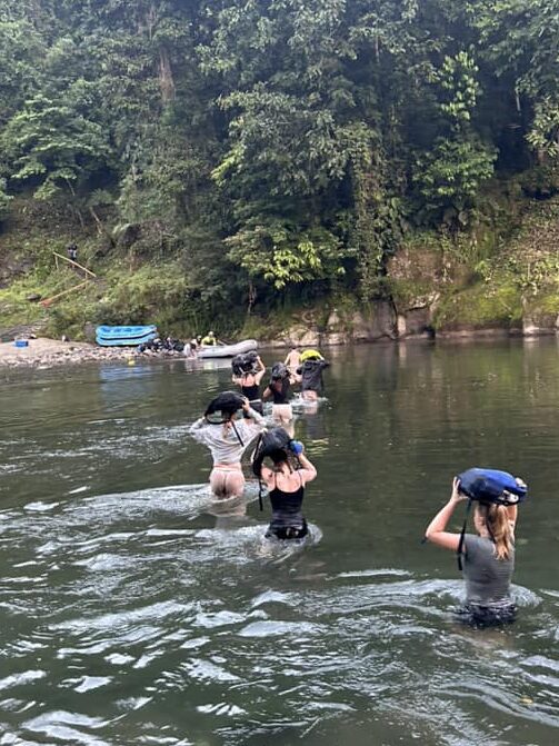 Students wear bags on their heads while walking through a river