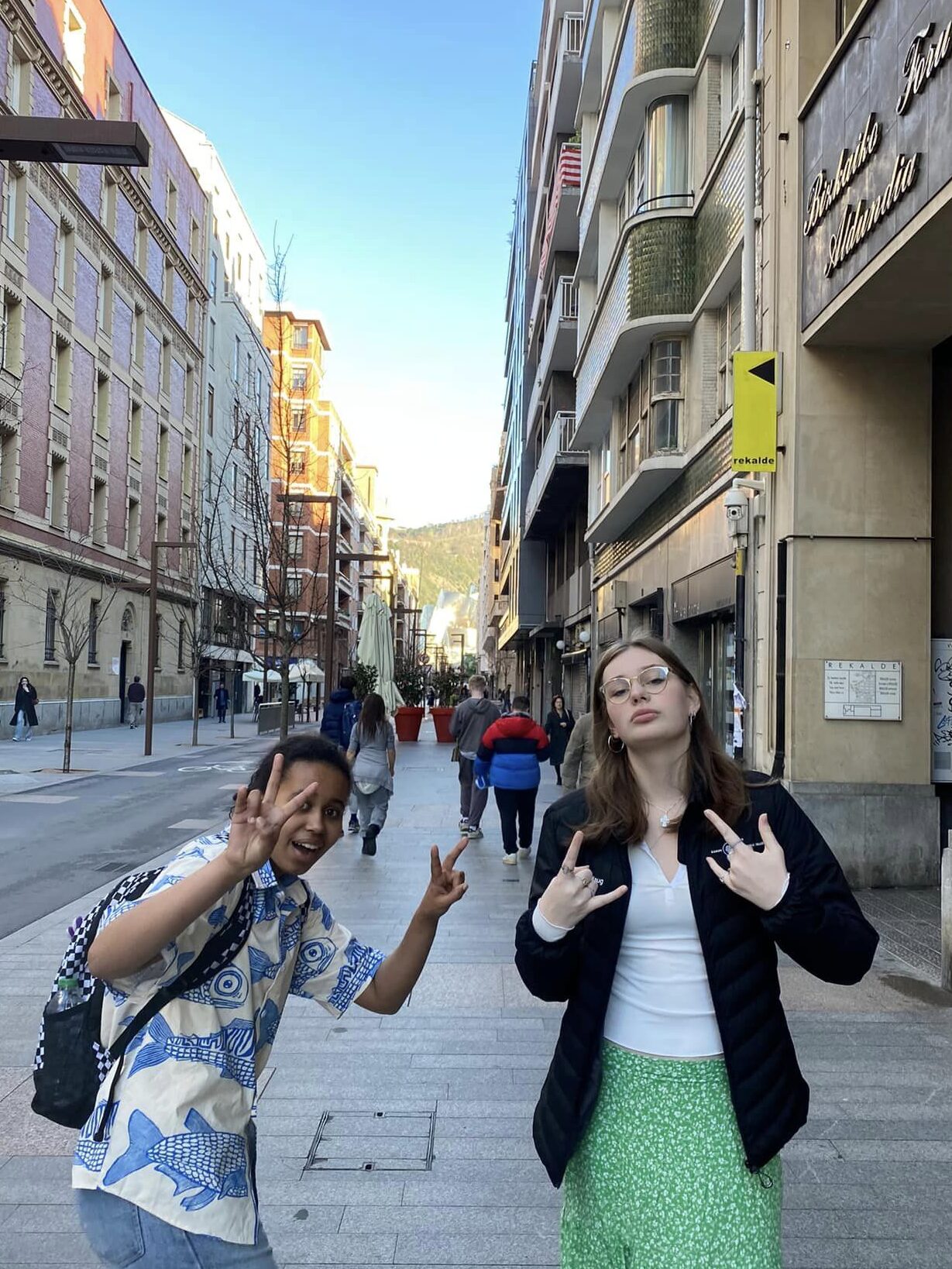 Two girls smiling and signalling to another