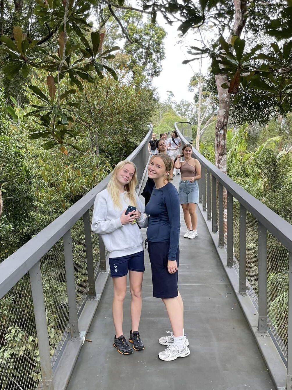 2 girls standing on a bridge with nature in the background