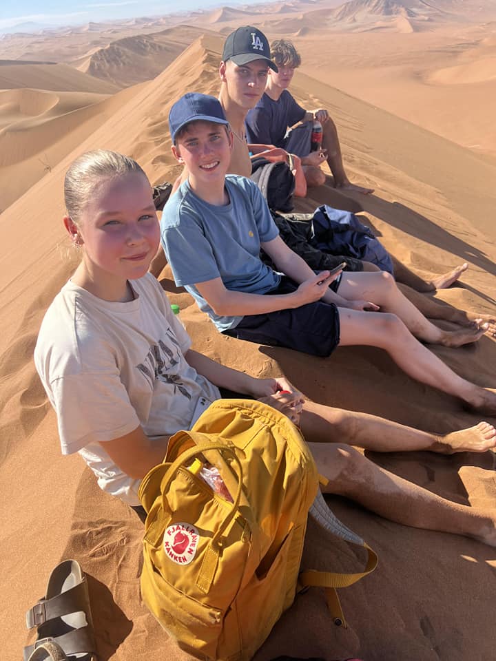 girls and boys sitting on a mountain of sand in the desert