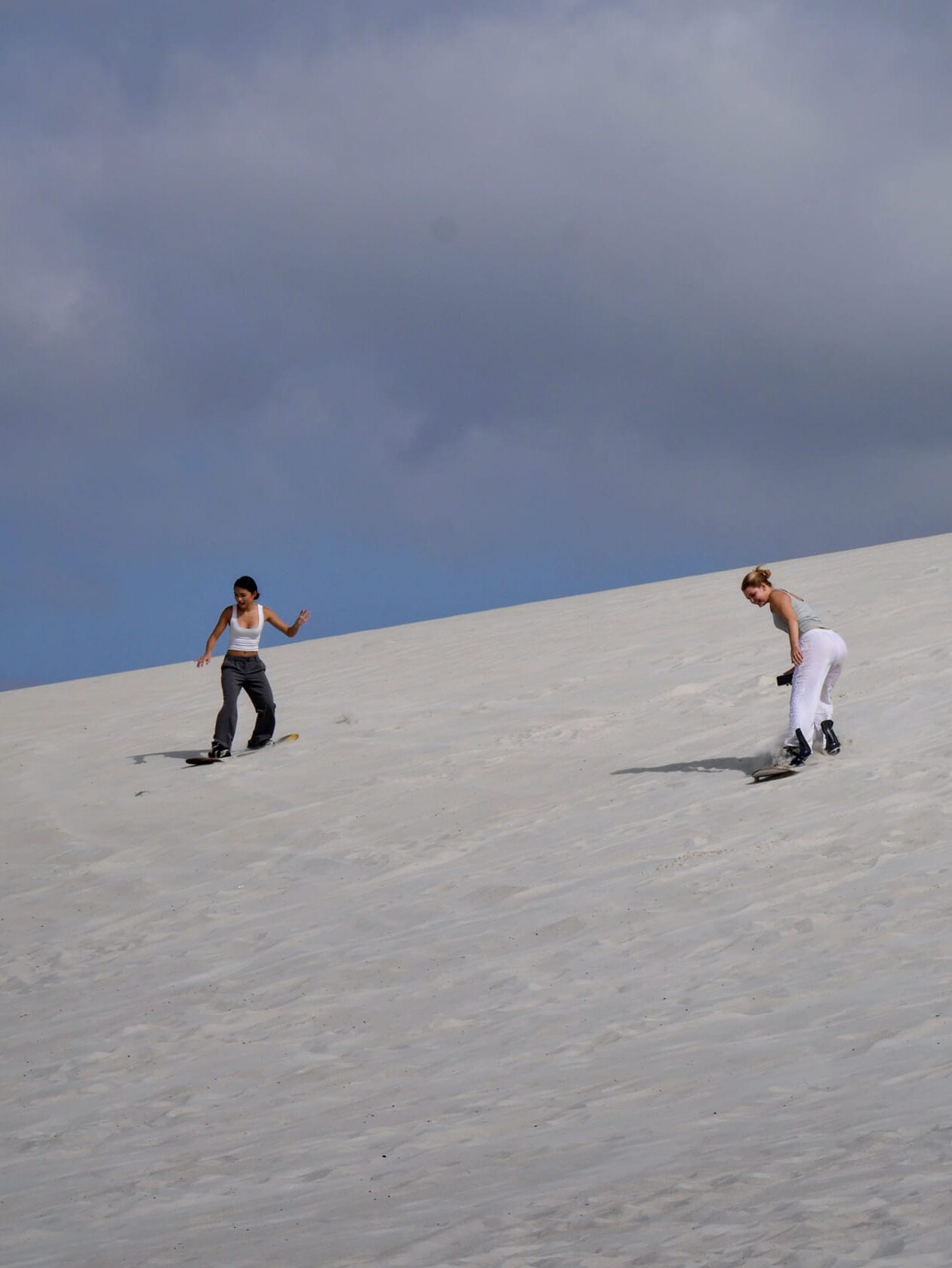2 piger surfer ned ad en bakke lavet af sand