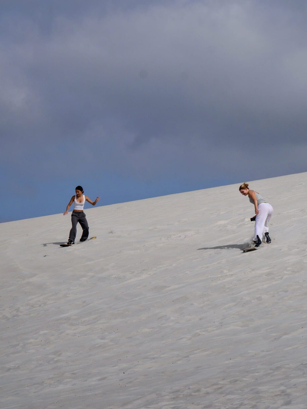 2 girls surfing down a hill made of sand