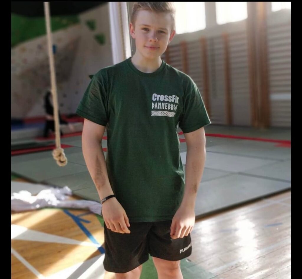 A boy stands in a green cross fit t-shirt and smiles