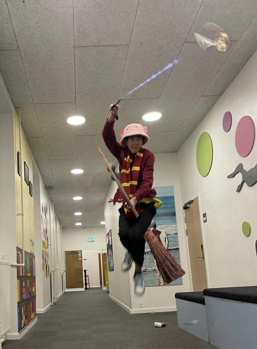 A boy sits on his flying broom trying to catch a ball