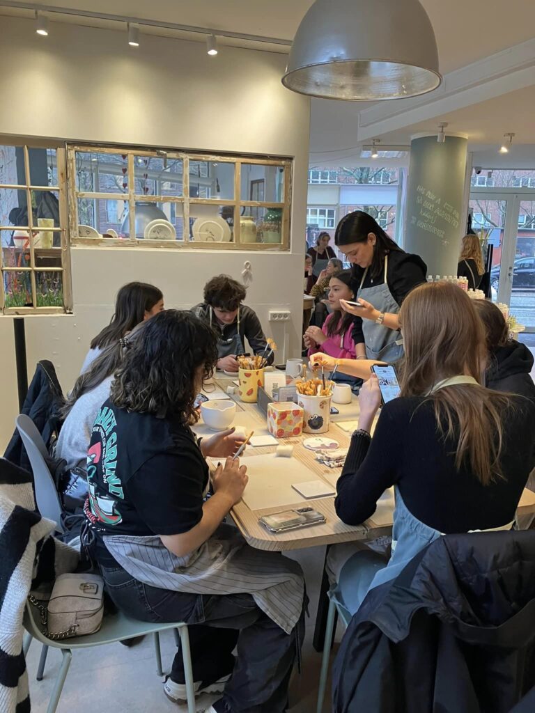 A group of young people sit around a table painting ceramics