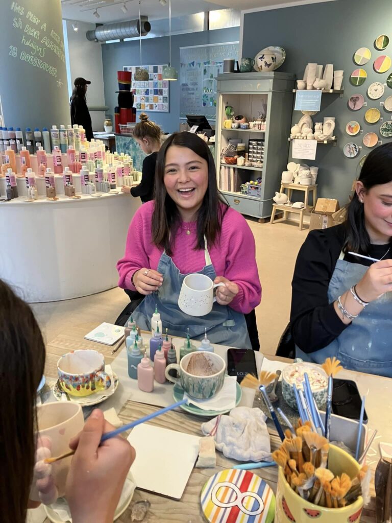 A girl sits at a table smiling with a cup in her hand.