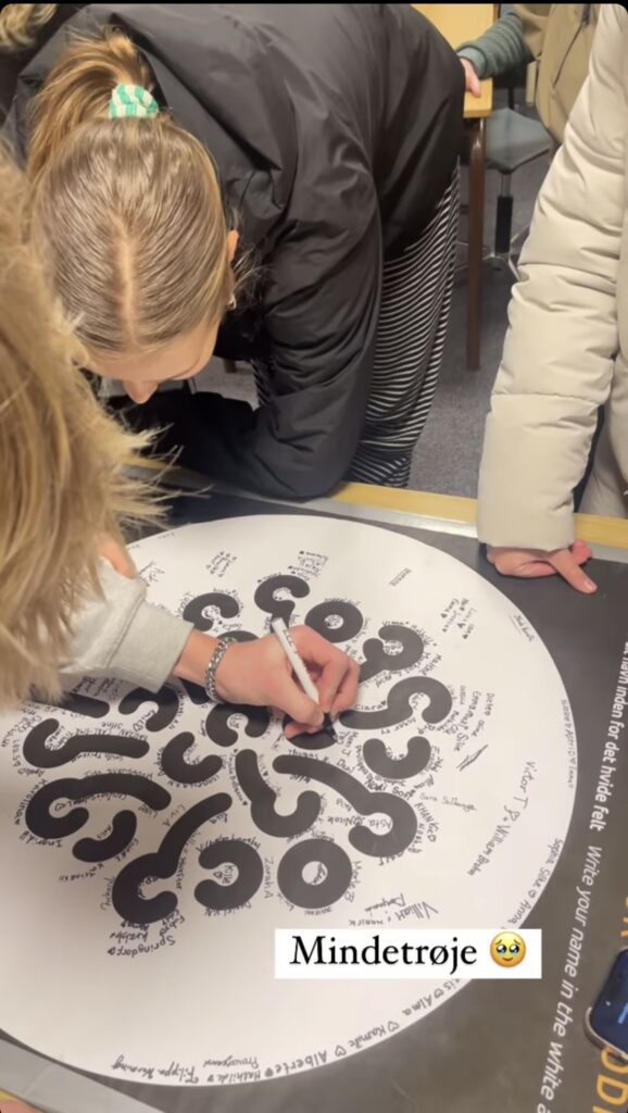 A group of students stand over a board with the Ranum efterskole college logo and write their names