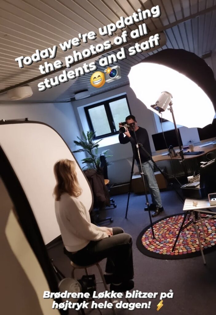 A girl sits on a chair with her back turned while a man takes her photo